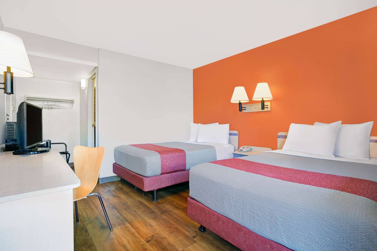 A hotel room with two beds, a desk, a chair, and a TV.