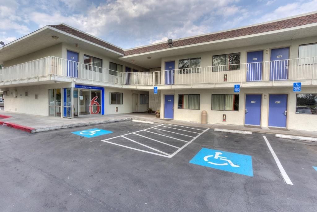 A building with a flat roof, a balcony on the second floor, and a parking lot with handicapped parking spaces.