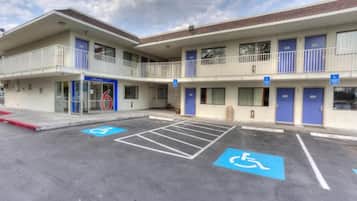 A building with a flat roof, a balcony on the second floor, and a parking lot with handicapped parking spaces.