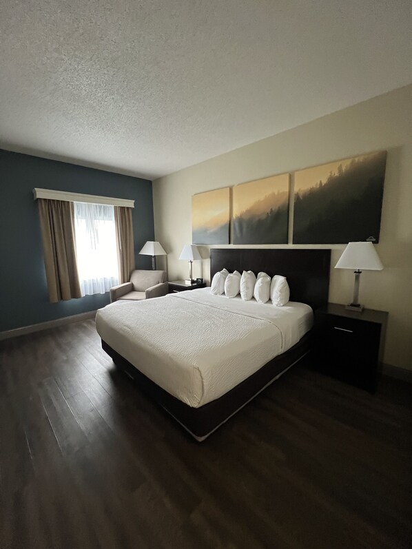 A hotel room with a large bed, two bedside tables, a nightstand, a window with curtains, and a wall-mounted painting. - Days Inn by Wyndham Penn State (State College)