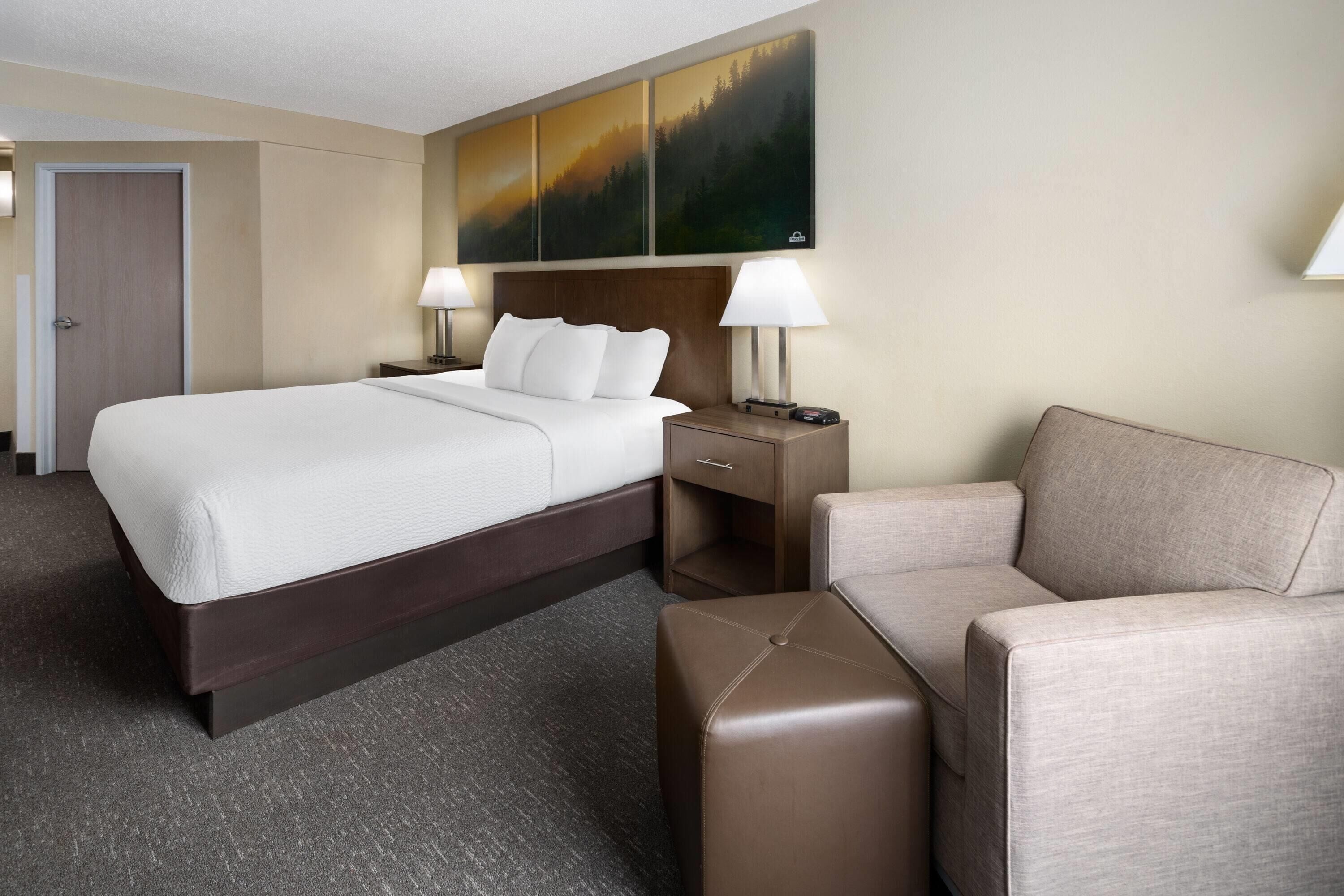 Ein Hotelzimmer mit einem großen Bett, zwei Nachttischen mit Lampen, einem Sofa und einem Gemälde an der Wand.