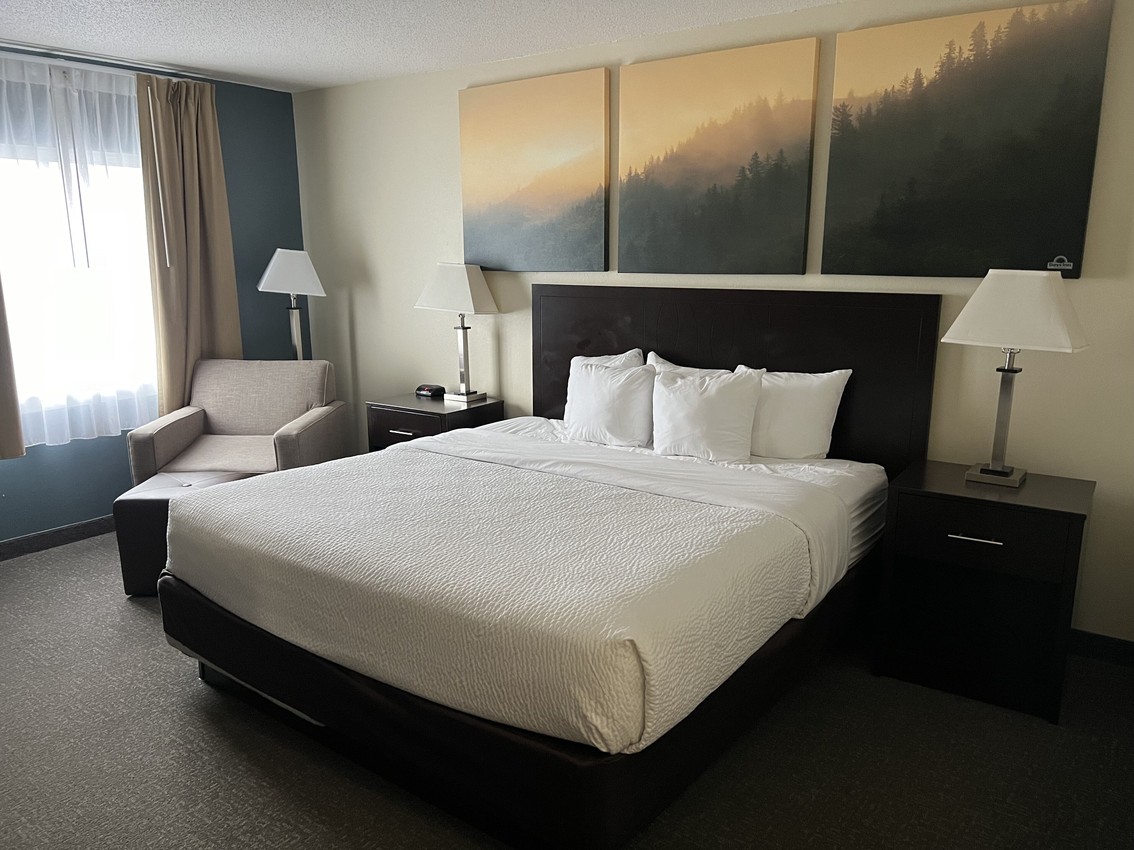 Ein Hotelzimmer mit einem großen Bett, einem Sessel, einem Nachttisch und einem Bild an der Wand.