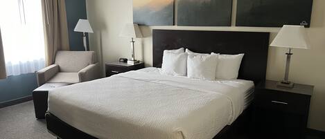 Ein Hotelzimmer mit einem großen Bett, einem Sessel, einem Nachttisch und einem Bild an der Wand.