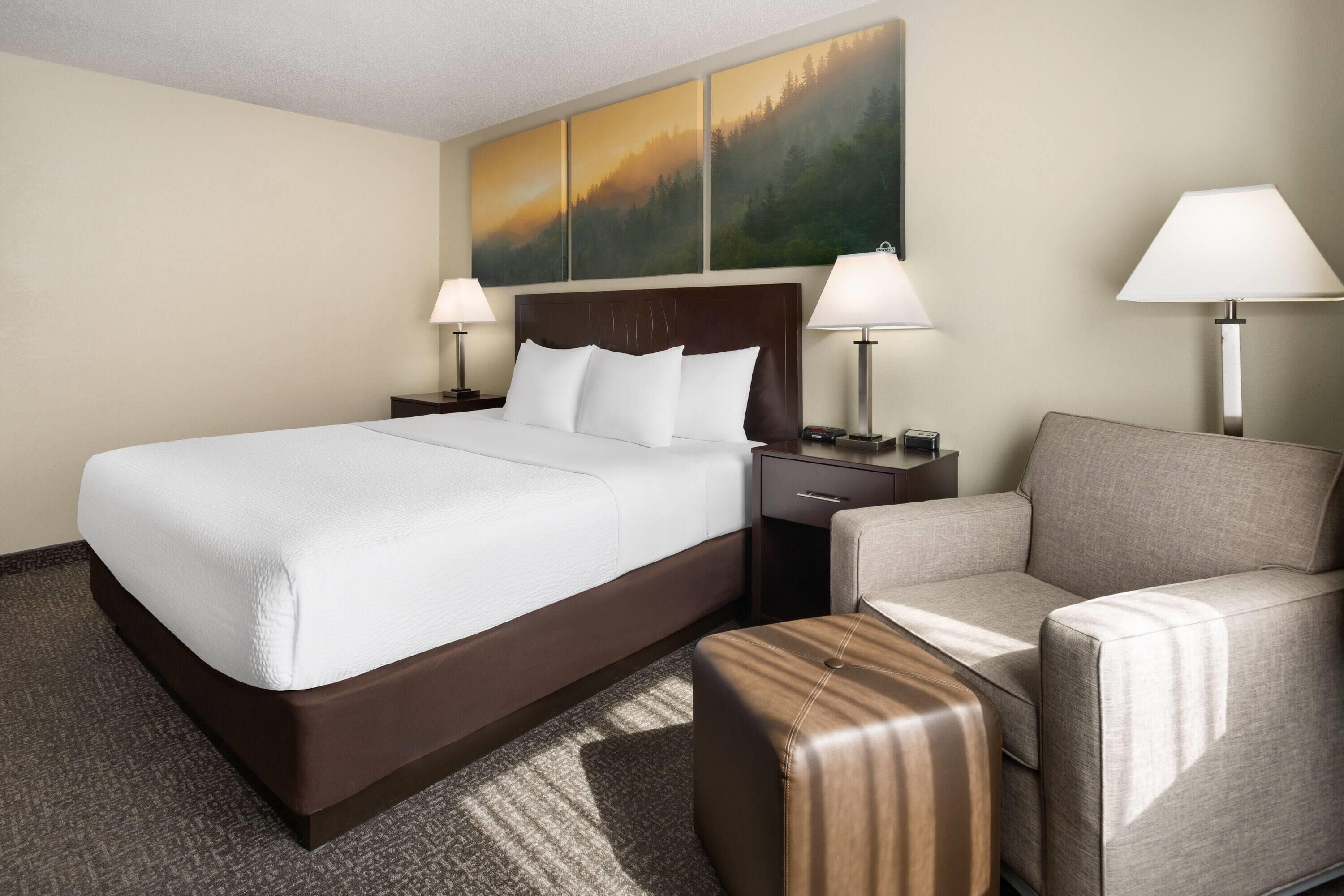 Una habitación de hotel con una cama grande, un sofá, una mesita de noche y una lámpara.