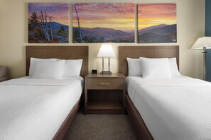 A hotel room with two beds, a nightstand with a lamp, and a wall-mounted painting of a sunset over mountains. - Days Inn by Wyndham Penn State (State College)