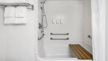Un baño blanco con ducha, dos barras para toallas, un tapete de baño de madera y dos botellas de champú.