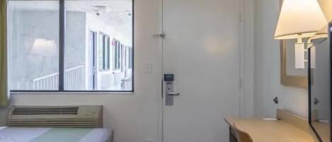 Una habitación de hotel con una cama, un escritorio, una silla, una lámpara y una puerta.