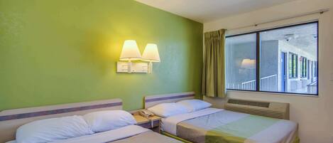 A hotel room with two beds, a nightstand with a phone, and a window with a view of a building.