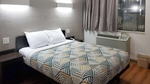 Una camera d'albergo con un letto, un condizionatore, una finestra con tende e un lampadario a parete.
