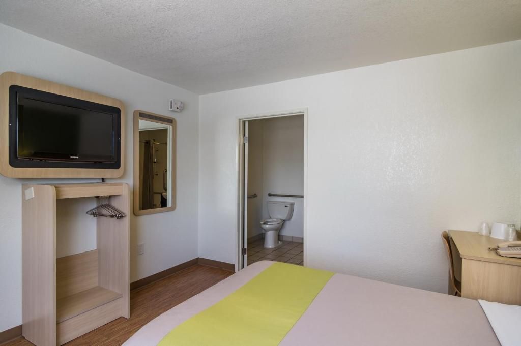 A hotel room with a bed, a television, a desk, and a bathroom visible through an open door.