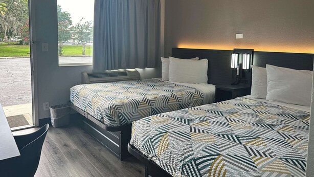 A hotel room with two beds, a desk, and a window with curtains. - Motel 6 Kissimmee, FL - Orlando (Kissimmee)