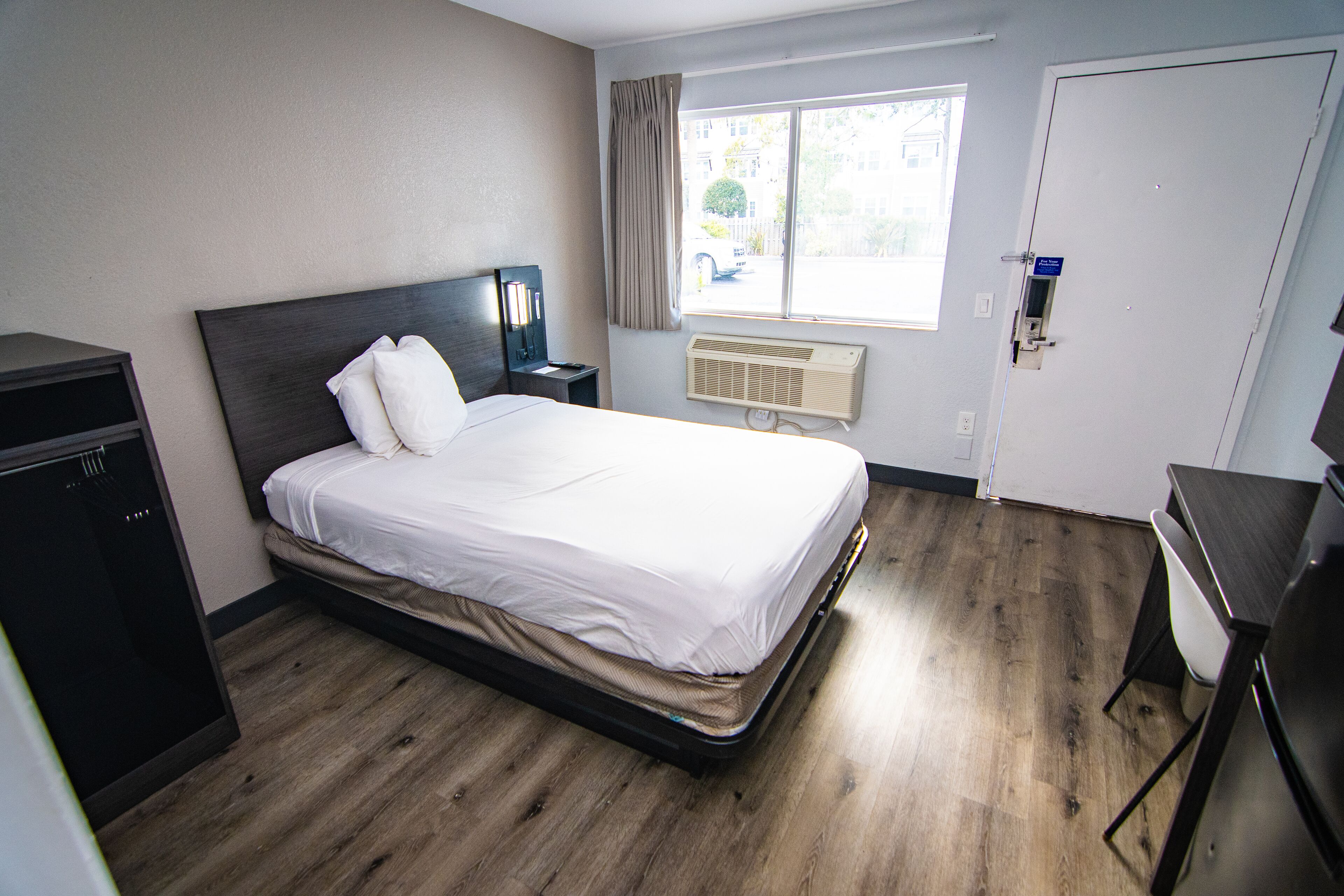 Une chambre d’hôtel comprenant un lit, un bureau, une chaise, une armoire, une fenêtre avec des rideaux et une porte.