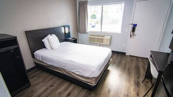 Une chambre d’hôtel comprenant un lit, un bureau, une chaise, une armoire, une fenêtre avec des rideaux et une porte.