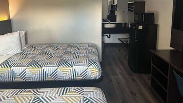Quarto de hotel com duas camas, uma kitchenette pequena e uma televisão.