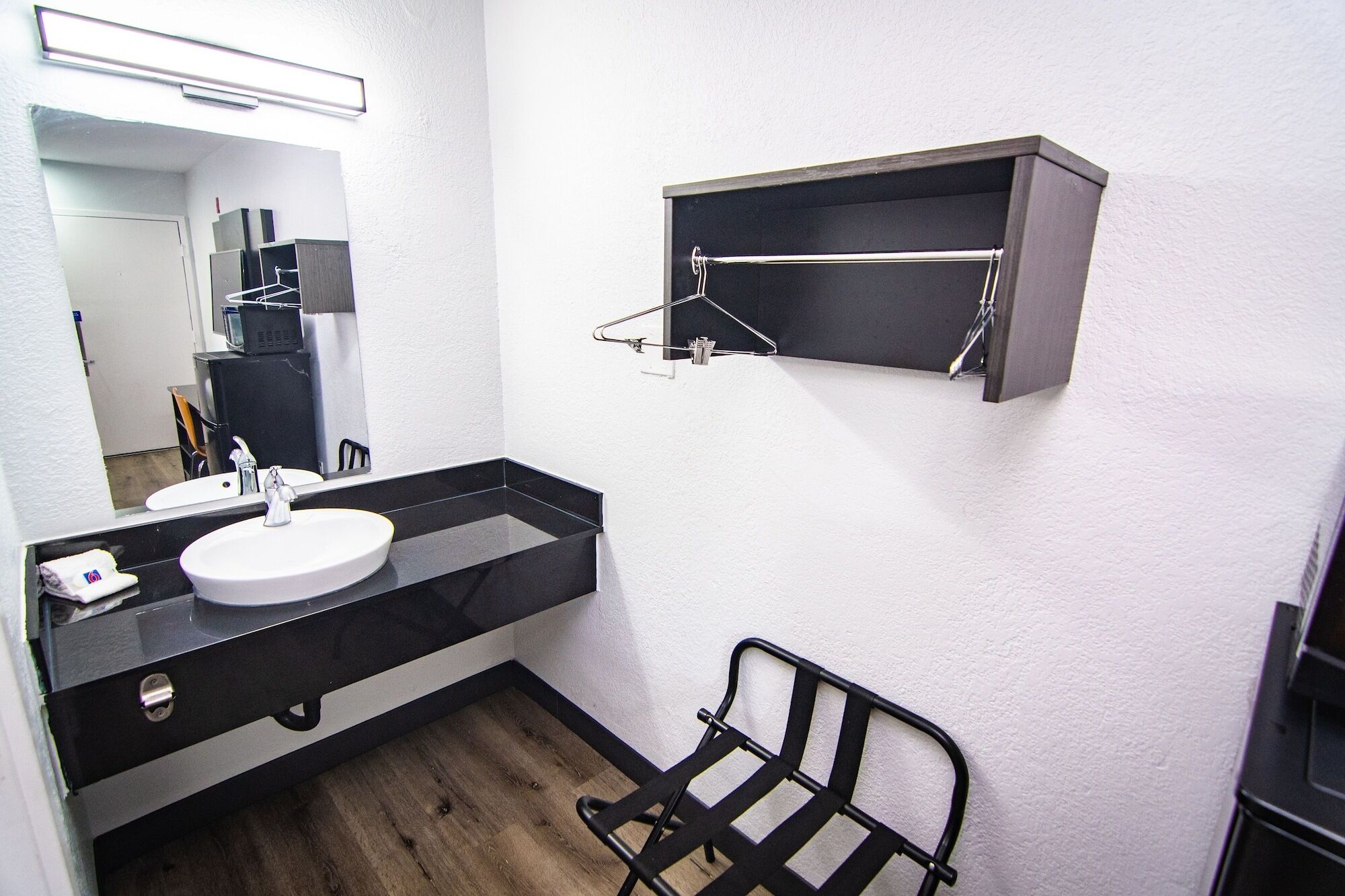 A bathroom with a white sink, black countertop, and a mirror. There is a black metal rack and a small shelf above the sink.