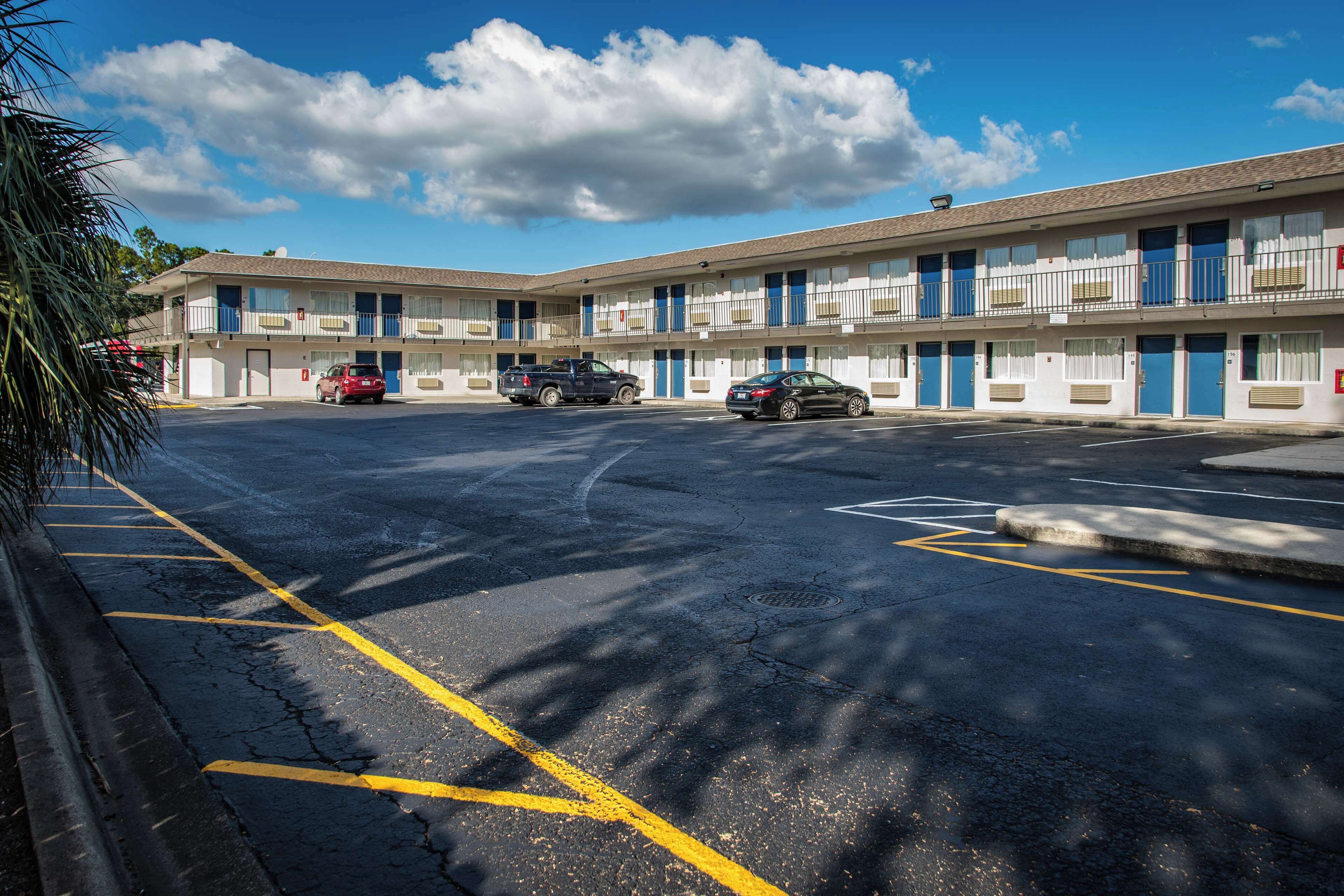 Ein Motel mit Parkplatz, mehreren Zimmern und blauem Himmel.