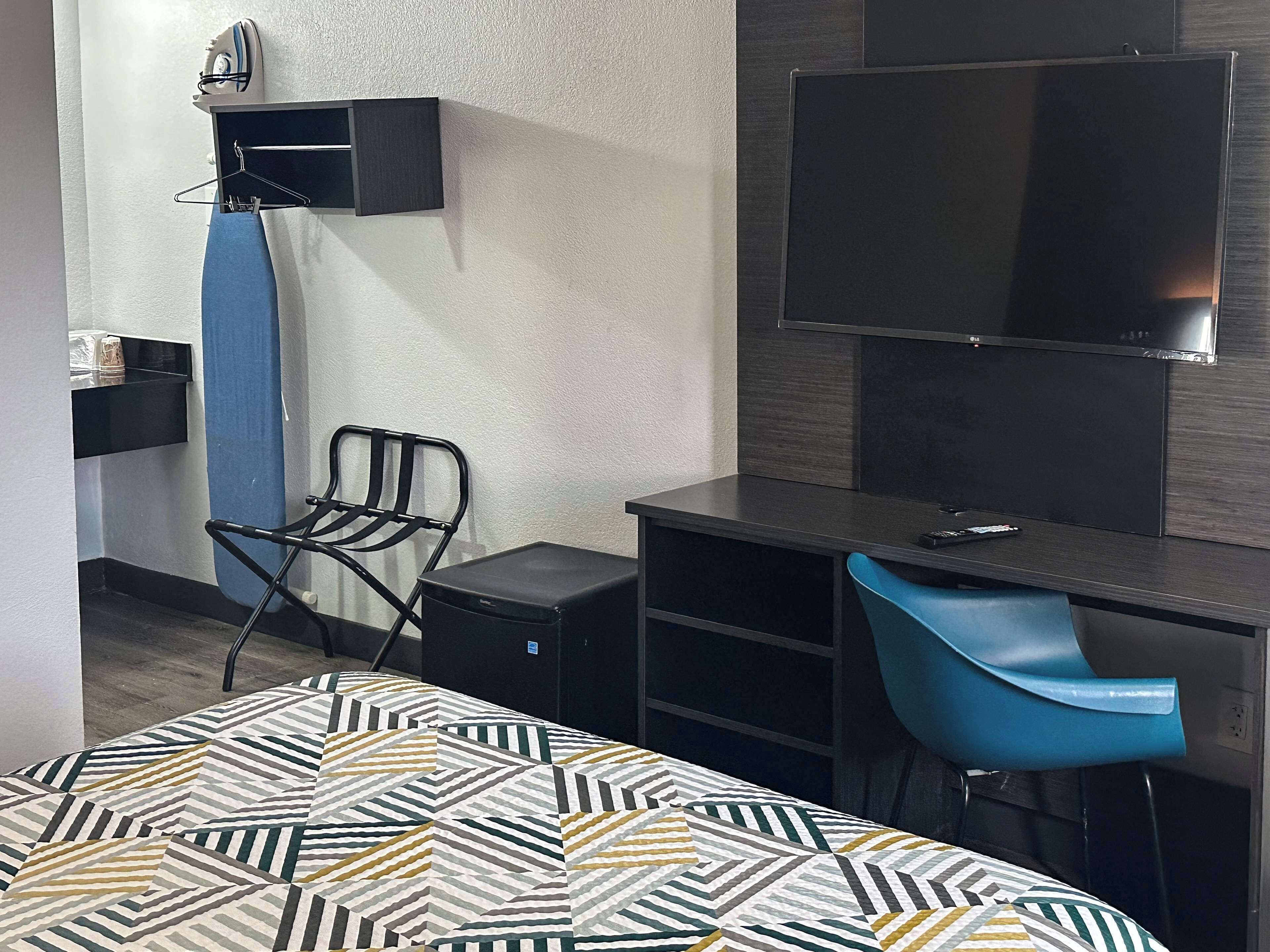 A hotel room with a bed, a desk, a chair, a TV, and a wall-mounted ironing board.