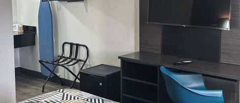 A hotel room with a bed, a desk, a chair, a TV, and a wall-mounted ironing board.