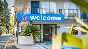 A hotel entrance with a '6 welcome' sign, a wheelchair-accessible ramp, and a potted plant. - Motel 6 Kissimmee, FL - Orlando (Kissimmee)