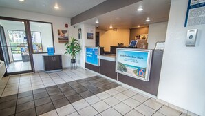 A reception area with a check-in counter, a potted plant, and informational posters. - Motel 6 Kissimmee, FL - Orlando (Kissimmee)