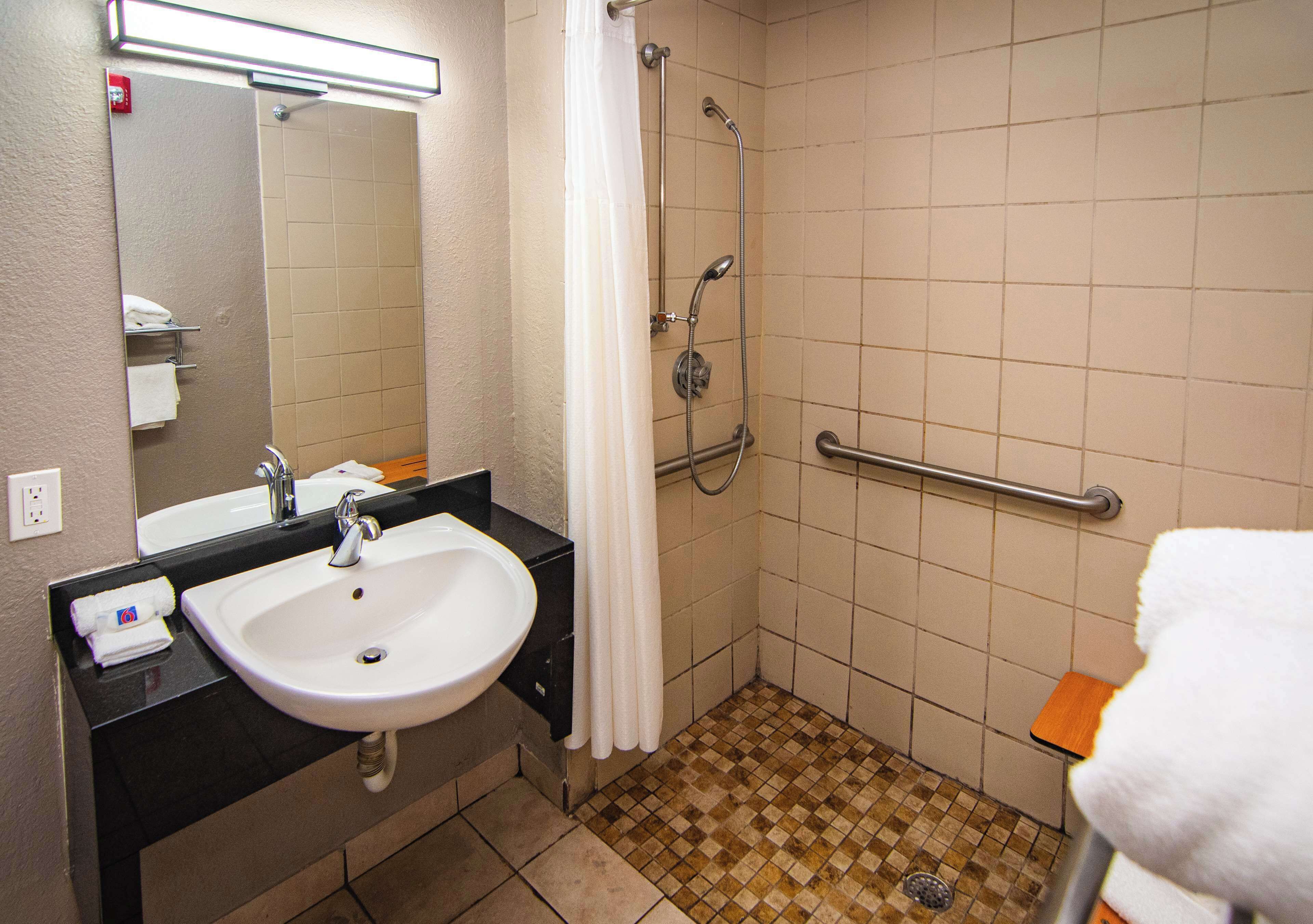 A bathroom with a sink, mirror, shower, and handrails.