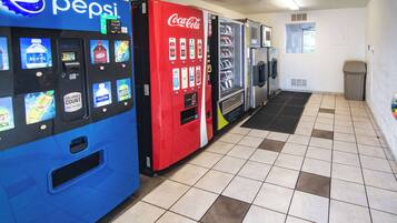 Une rangée de distributeurs automatiques proposant diverses boissons, notamment du Coca-Cola et de l’eau Aquafina, dans une pièce carrelée.