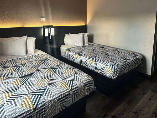 A hotel room with two single beds, each with patterned bedding, a nightstand, and wall-mounted reading lamps. - Motel 6 Kissimmee, FL - Orlando (Kissimmee)