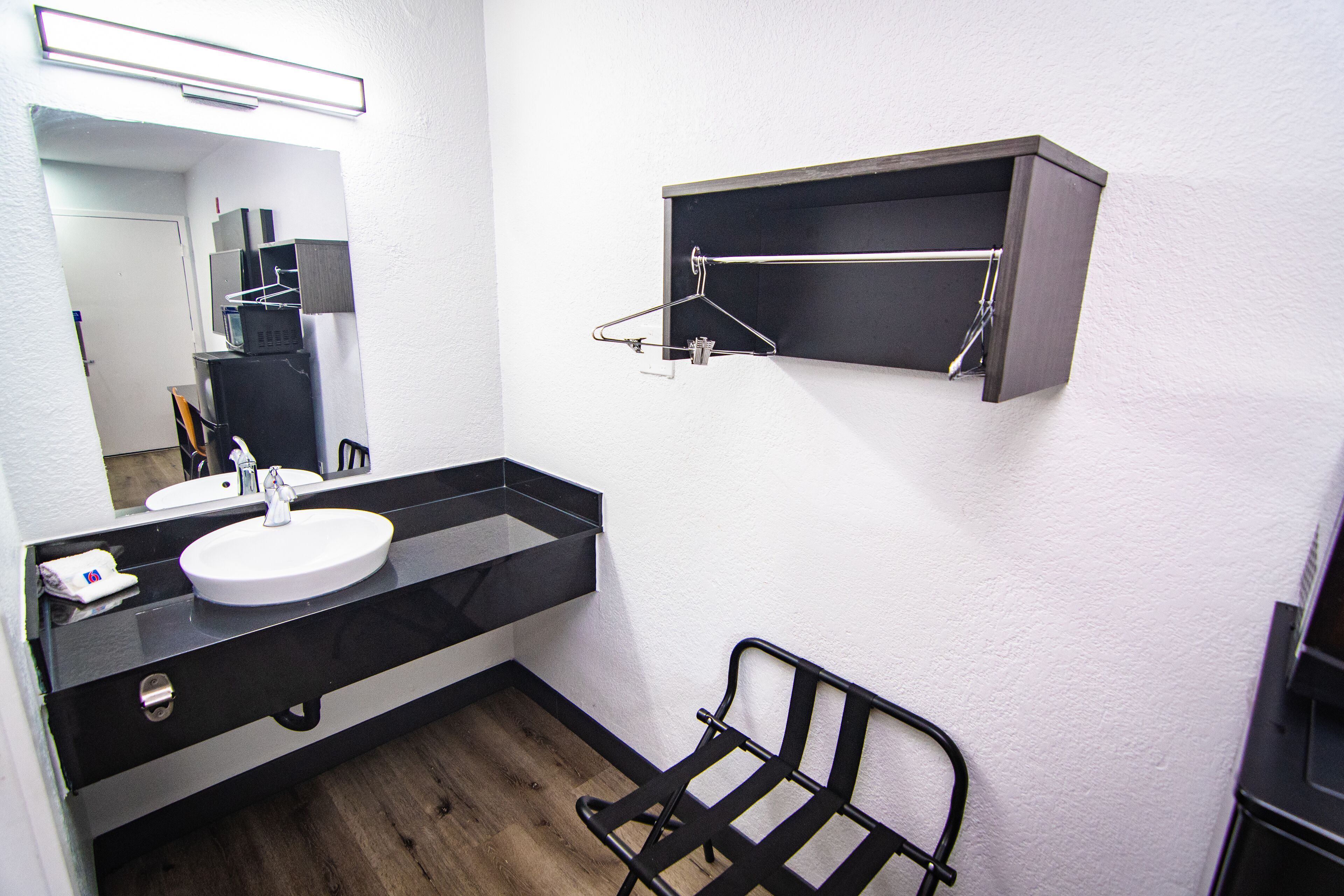 Casa de banho moderna com bancada preta, lavatório branco e espelho em cima. Há uma estante de metal preto e um pequeno prateleira acima do lavatório.