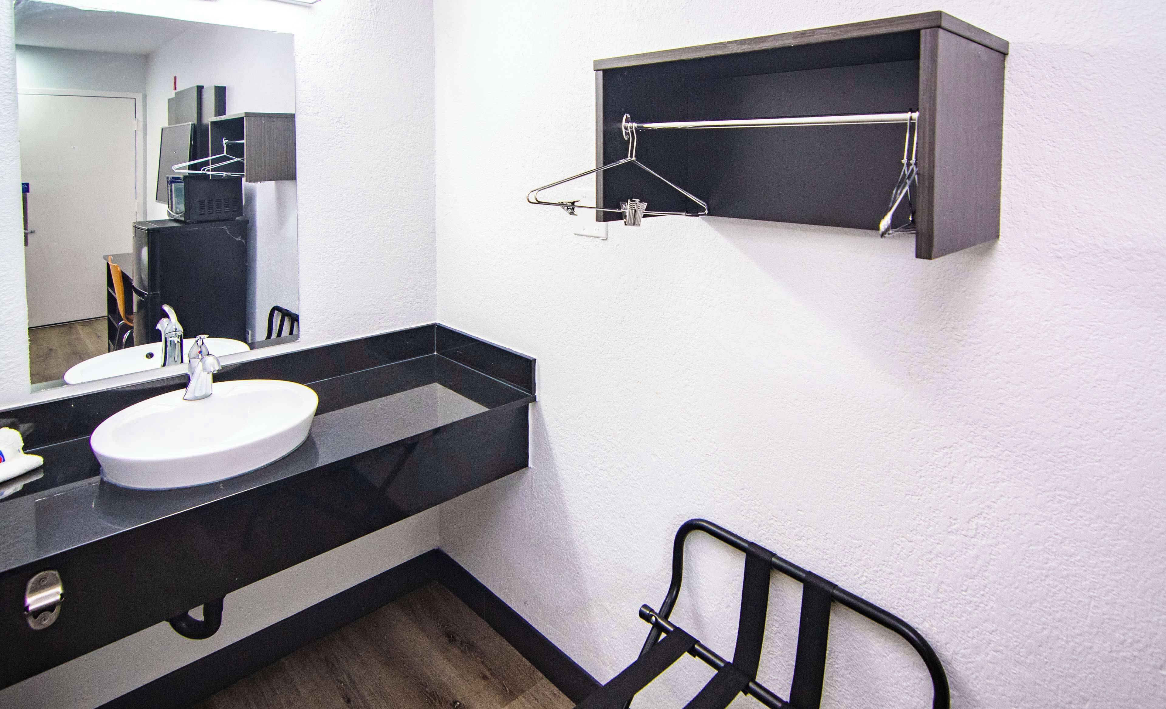 A modern bathroom with a white sink, black countertop, and a mirror. There is a black metal chair and a medicine cabinet on the wall.