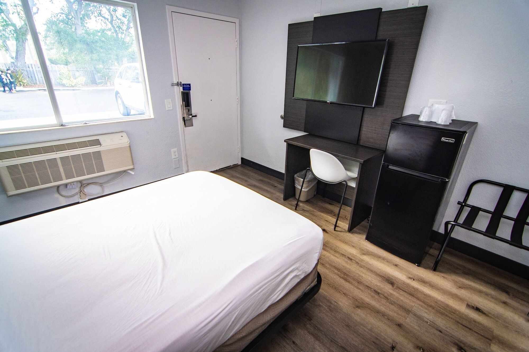 Een hotelkamer met een bed, een bureau met stoel, een televisie en een koelkast.