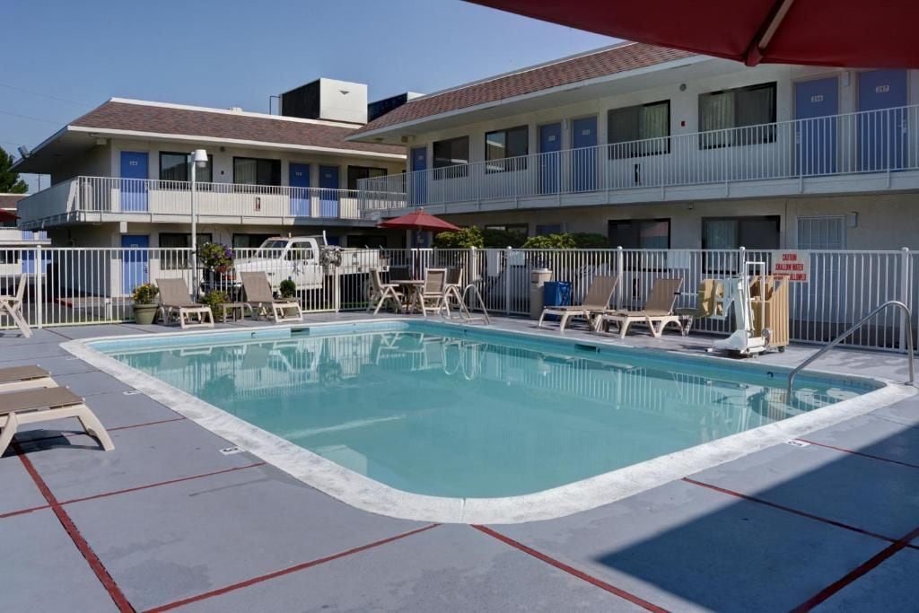 A swimming pool with lounge chairs, a covered area, and a multi-story building with balconies.