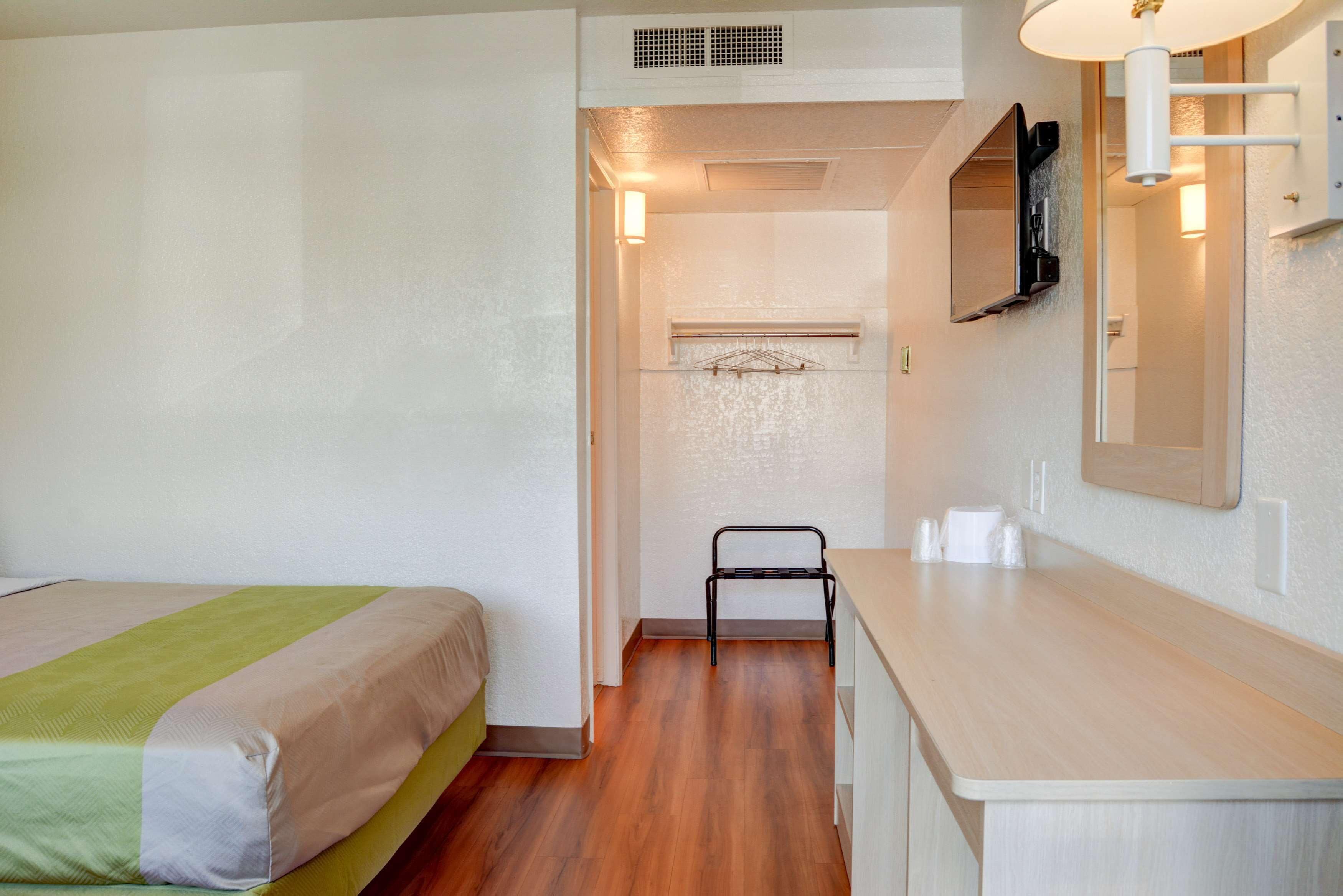 A hotel room with a bed, a small desk, a mirror, and a shower area.