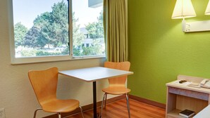 Habitación de hotel con ventana, dos sillas, una mesita, una lámpara y mesita de noche con teléfono y libro.