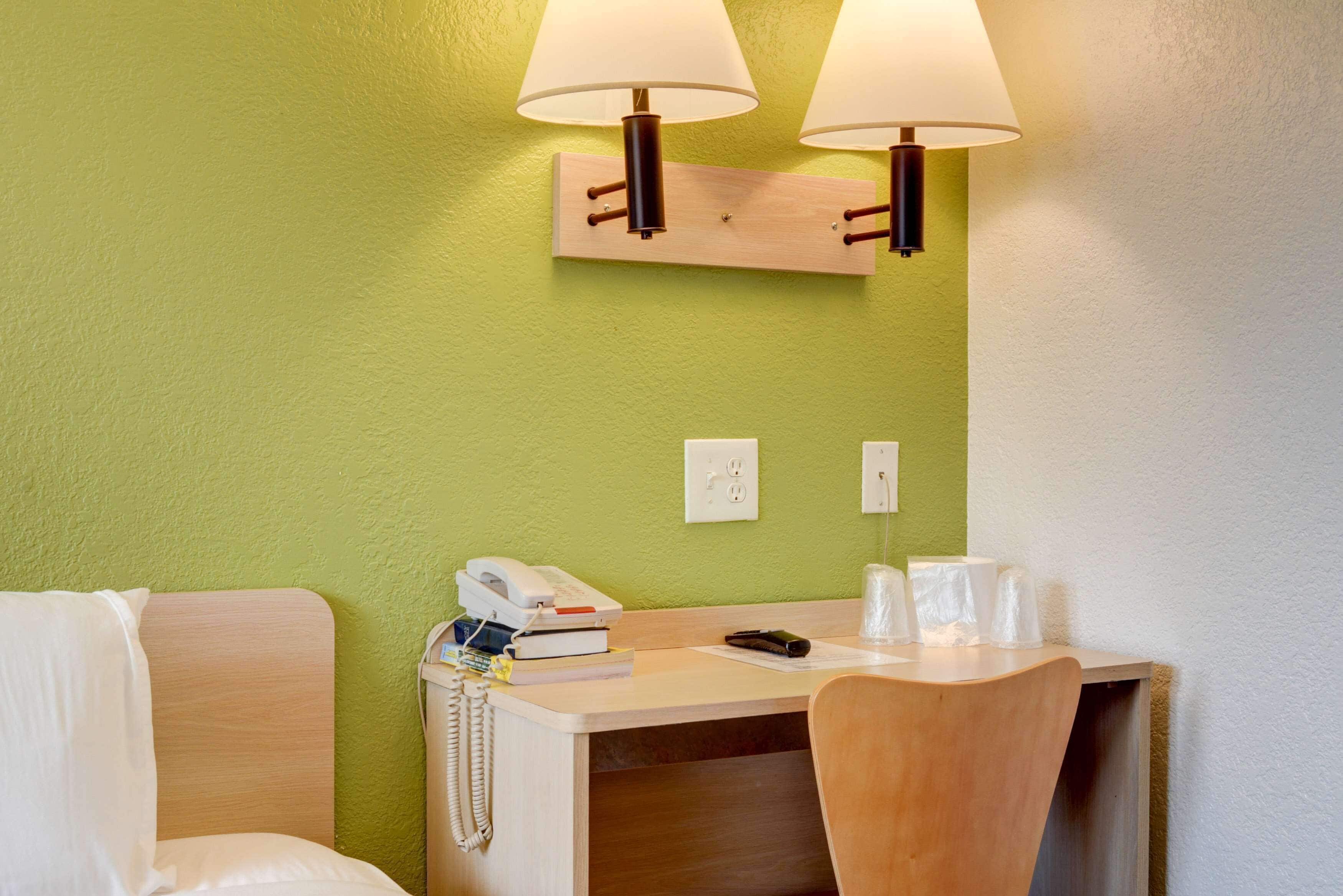 A hotel room with a desk, two lamps, a telephone, and a chair.