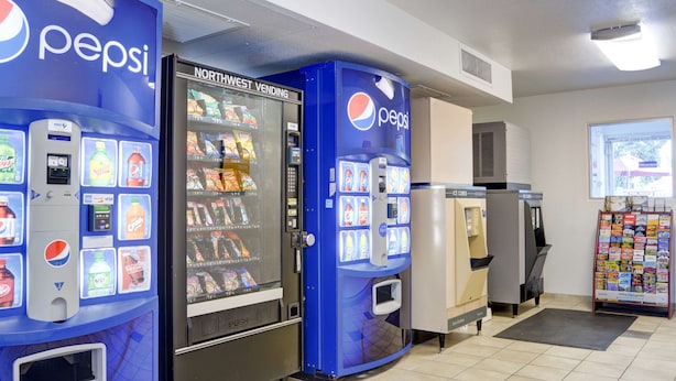 Un área de venta automática con máquinas de Pepsi y Northwest, dispensadores de hielo y un estante de revistas.