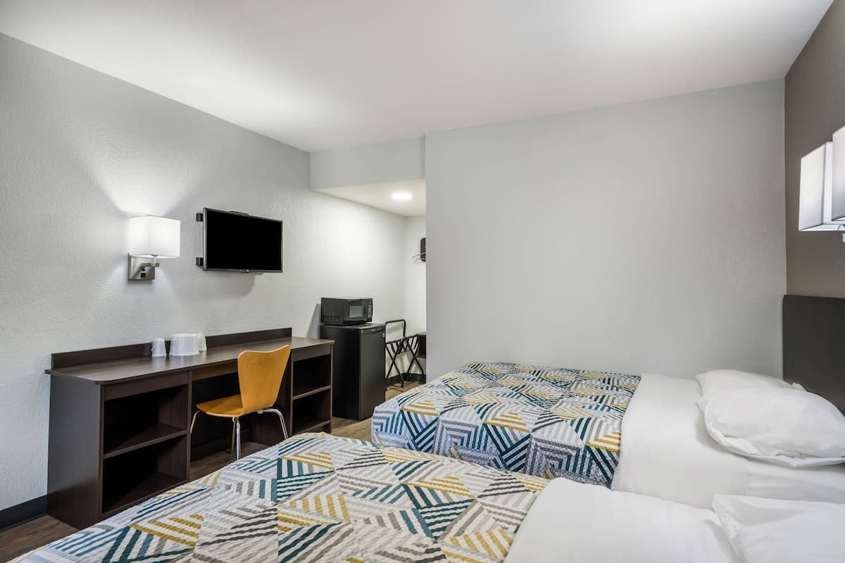 A hotel room with two beds, a desk, a chair, a TV, and a microwave.