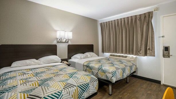 A hotel room with two beds, a nightstand, a lamp, a window with curtains, and a door. - Motel 6 Sandston, VA - Richmond, Va (Sandston)