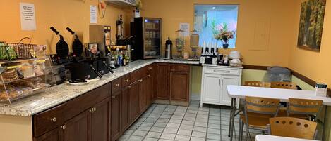 A kitchen with a counter, cabinets, a refrigerator, and a dining area with chairs and a table.
