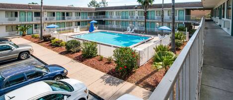 Un motel con piscina, varios balcones y coches aparcados.