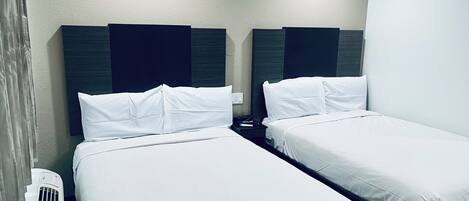 Habitación de hotel con dos camas individuales, cada una con ropa de cama blanca y cabeceros oscuros.