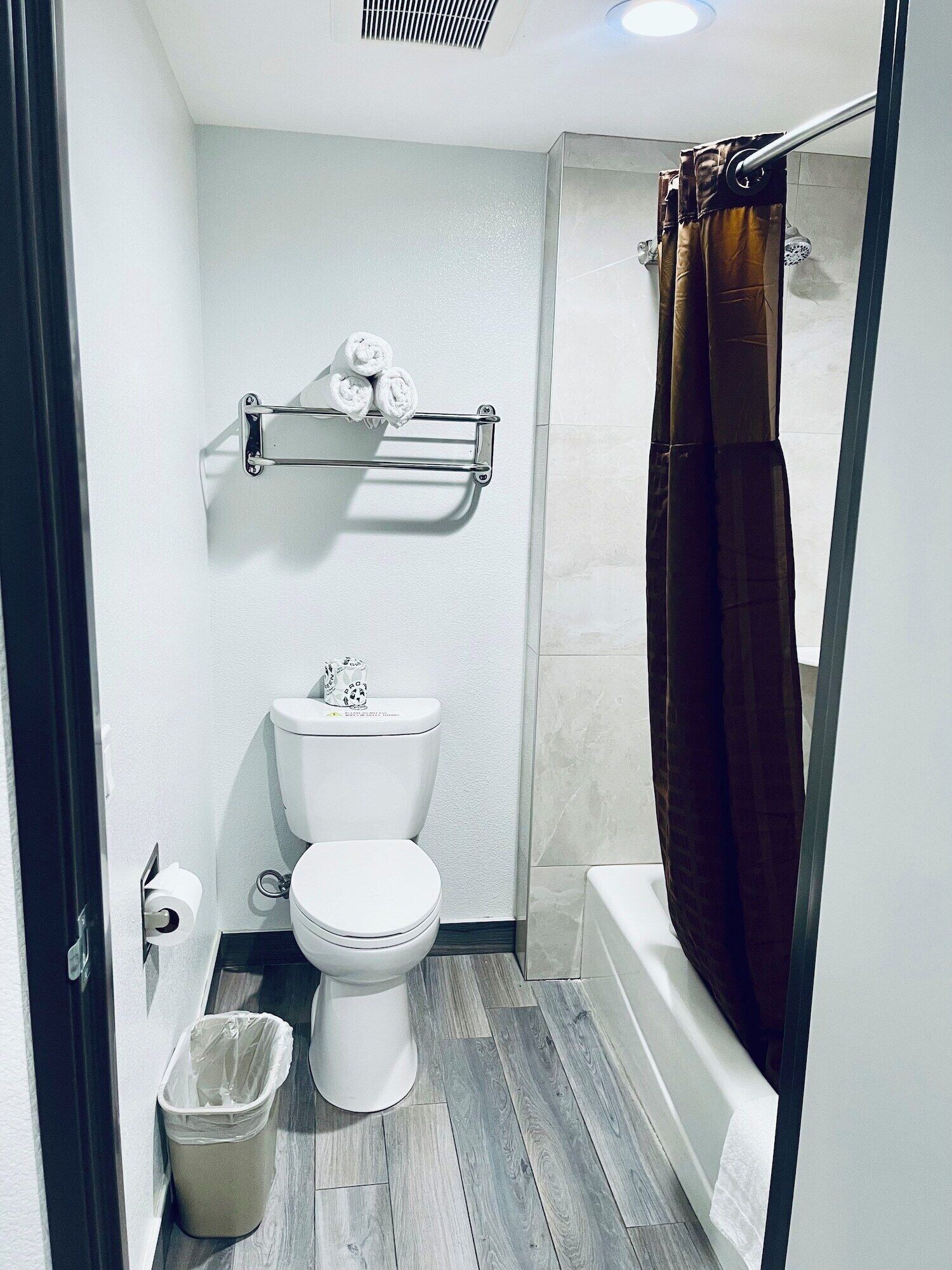 Un baño con inodoro, toallero, cortina de ducha y cubo de basura.