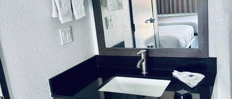 Un baño moderno con un lavabo negro, un espejo y un perchero para toallas.