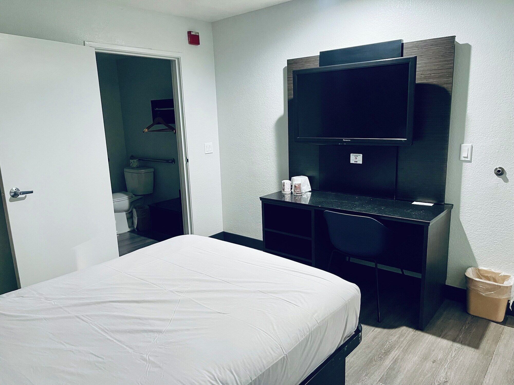 Una habitación de hotel con una cama, un escritorio con una silla, un televisor y un cubo de basura.