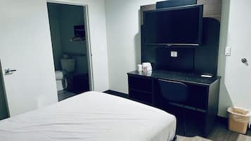 Una habitación de hotel con una cama, un escritorio con una silla, un televisor y un cubo de basura.