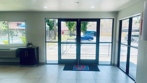 A hotel lobby with a tiled floor, a reception desk, and a view of the parking area through glass doors.