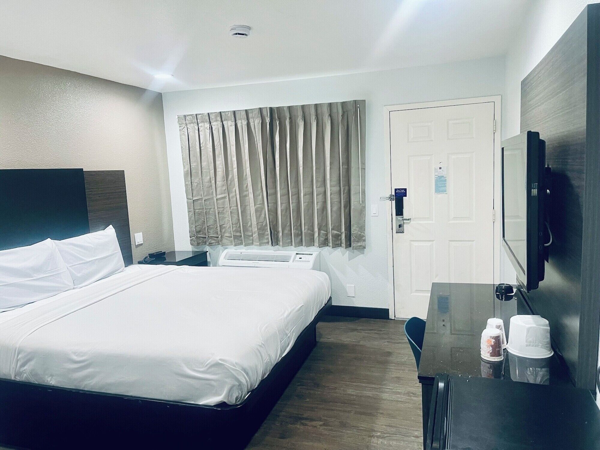 Una habitación de hotel con cama, escritorio, silla, televisor y puerta.