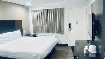 Una habitación de hotel con cama, escritorio, silla, televisor y puerta.