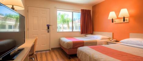 A hotel room with two beds, a desk with a TV, a window with a view of palm trees, and two wall-mounted lamps.