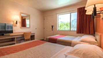 A hotel room with two beds, a desk with a television, a chair, and a window with curtains.