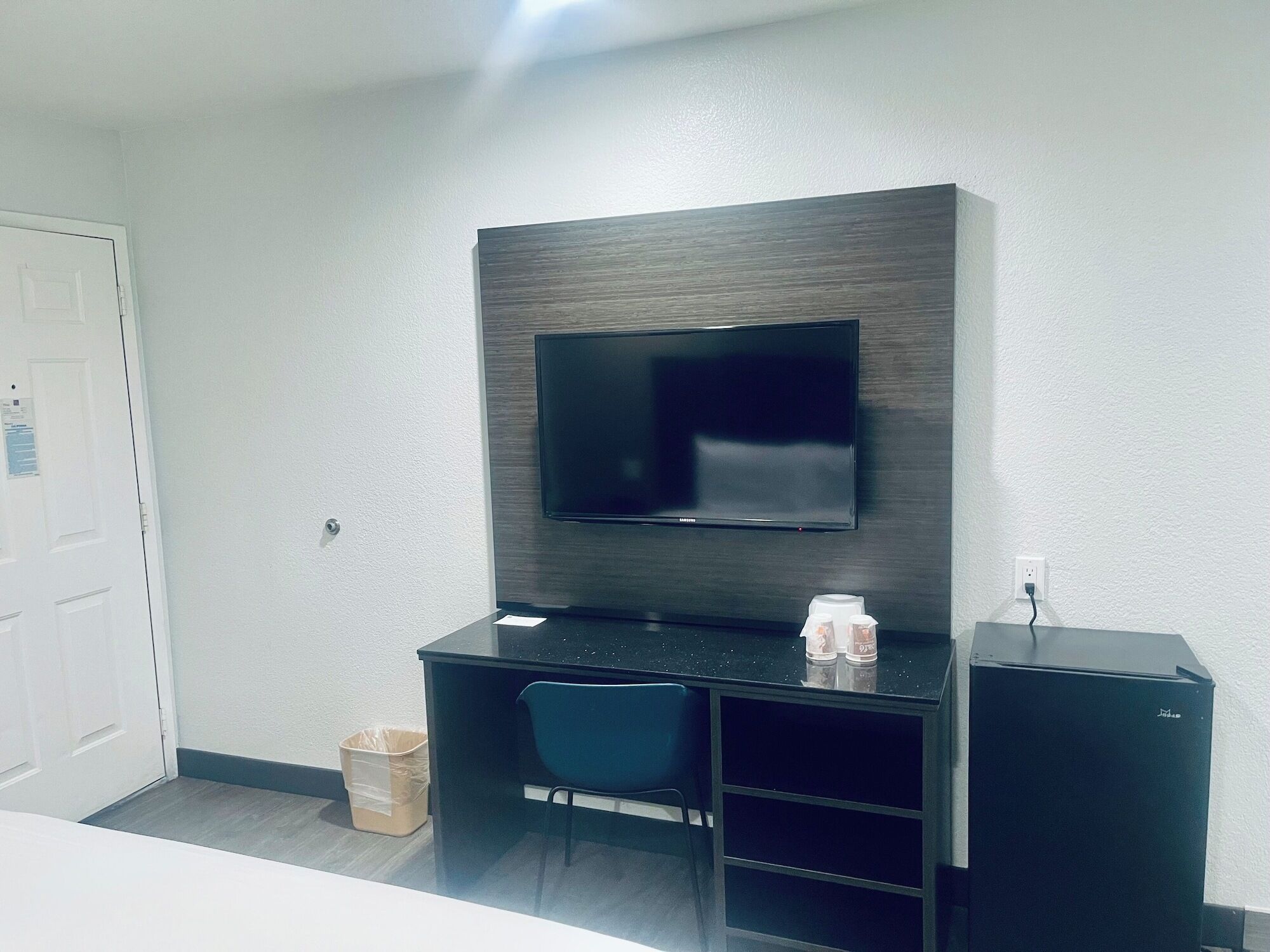 A modern room with a flat-screen TV mounted on a dark wall, a desk with a chair, and a small cabinet.